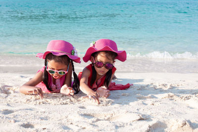 Girls playing with sand while lying at beach