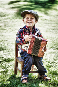 Full length of boy holding accordion while sitting on chair at land