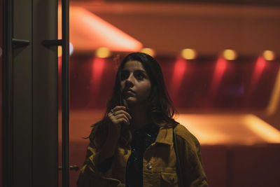 Young woman looking away while standing against illuminated lights at night