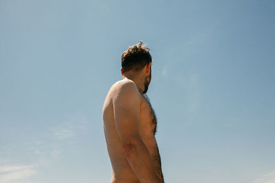 Side view of shirtless young man against blue sky