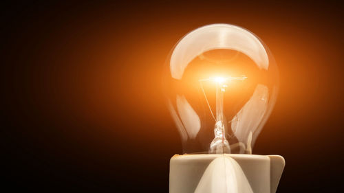 Close-up of illuminated light bulb against colored background