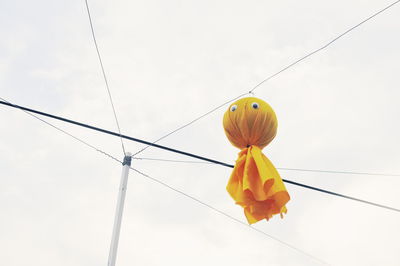 Low angle view of yellow decoration hanging from cable against sky 