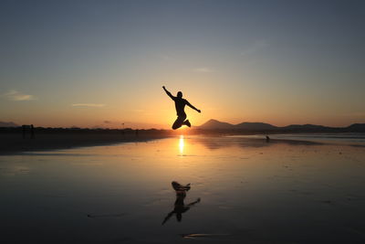 Silhouette man jumping on shore against sky during sunset