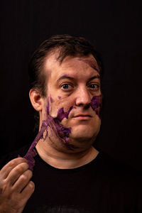 Portrait of man peeling of make-up against black background