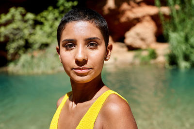 Young hispanic woman with short hair looking at camera on blurred background of lake on summer weekend day