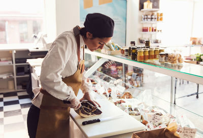 Female owner cutting meat at counter in grocery store