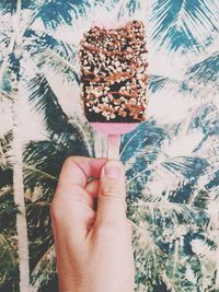 Cropped image of hand holding sweet food against wall with mural