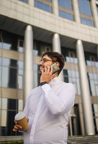 Young businessman using mobile phone near building