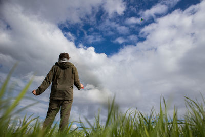 Rear view of man walking on field against sky