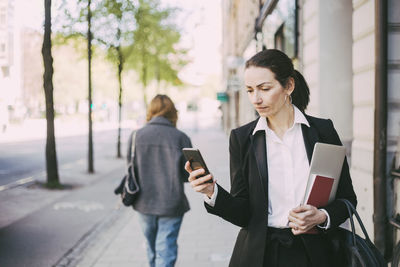 Woman holding mobile phone while standing on laptop