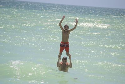 Happy father lifting son while enjoying in sea on sunny day