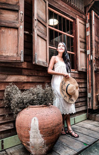 Full length of woman holding hat standing by window