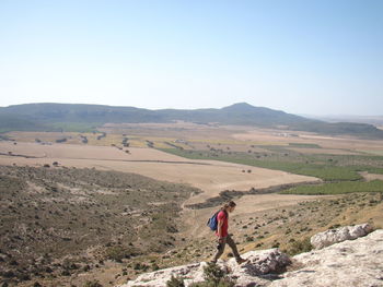 Rear view of man hiking in desert against clear sky