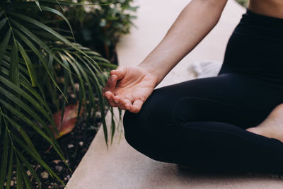Low section of woman sitting on footpath on lotus position and the hand on a mudra 