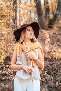 Young woman wearing hat standing in forest during autumn