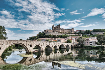 Arch bridge over river by buildings against sky