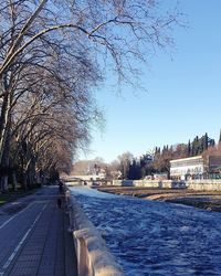 Road by canal in city against clear sky