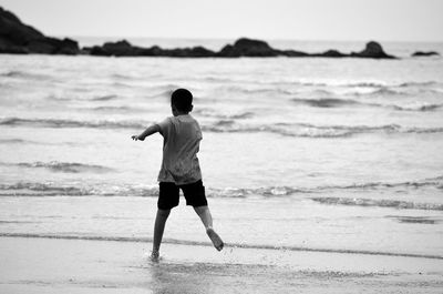 Rear view of boy running at beach against sky