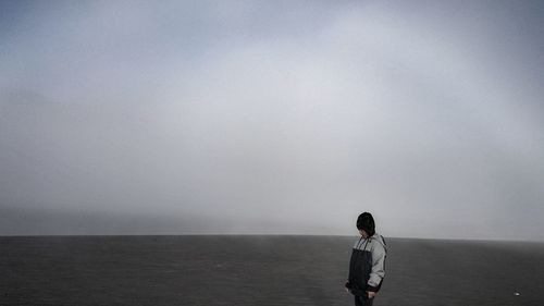 Rear view of man standing on sea against sky