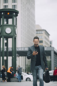 Mature businessman using mobile phone while walking on street in city