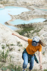 Happy young woman traveler in cap running on sand of clay quarry with blue turquoise water landscape