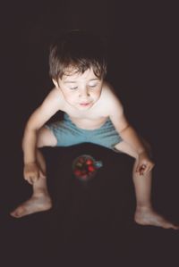 Cute shirtless boy with fruit sitting against black background