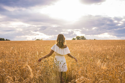 Rear view of woman standing in field against sky