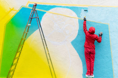 Rear view of young woman painting wall