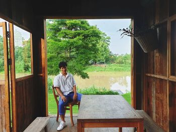 Smiling man sitting on chair in cottage by lake