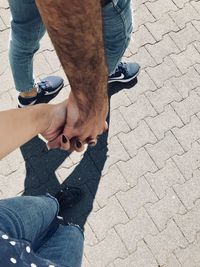 Low section of couple holding hands while walking on footpath