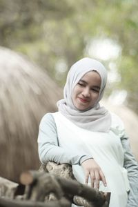 Smiling young woman wearing hijab leaning on wooden railing