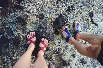 Low section of man and woman wearing sandal while standing on rock