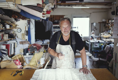 Portrait of senior male owner standing with fabric at workbench in workshop