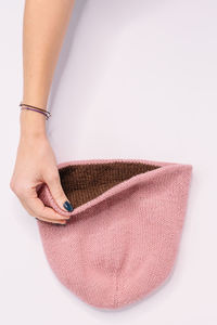 Hand of caucasian woman hold bilateral pink-brown knitted beanie hat. flat lay, copy space. 