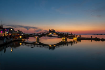 Illuminated bridge over river against sky at sunset