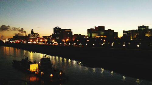 Illuminated city by river against clear sky at night