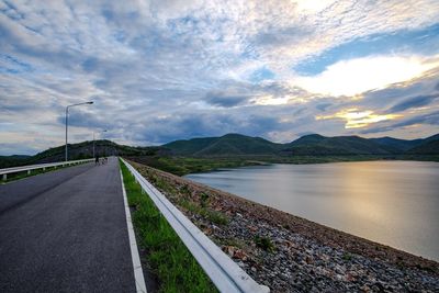 Road by lake against cloudy sky during sunset
