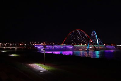 Illuminated ferris wheel in city against clear sky at night