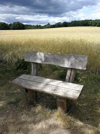 Empty bench on field against sky