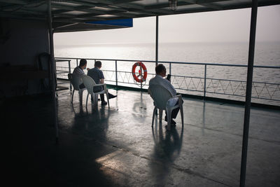 Rear view of people sitting on railing by sea