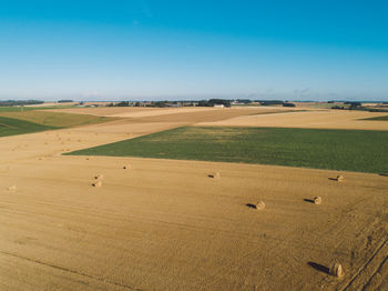 High angle view of hay bales on agricultural field against blue sky