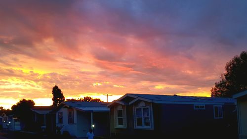 Silhouette of houses against cloudy sky at sunset