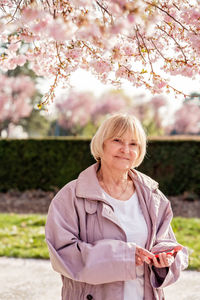 Portrait of senior woman with smartphone thoughtfully looking at camera outdoors. pensioner in park