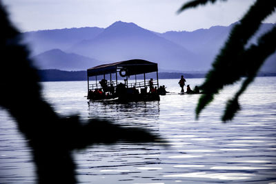 Silhouette people on boat in lake against sky