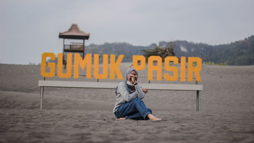 Full length of woman sitting at beach with text in background