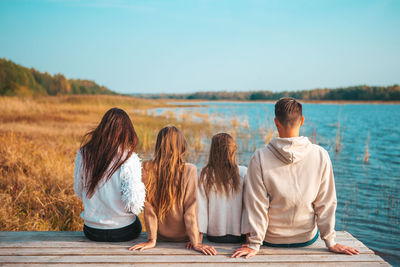 Rear view of friends sitting on shore against sky