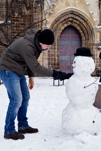 Man touching snowman while standing outdoors during winter