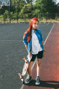 Portrait of a charming girl with a skateboard in her hand on a sports field