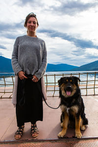 Portrait of woman with dog standing against sky