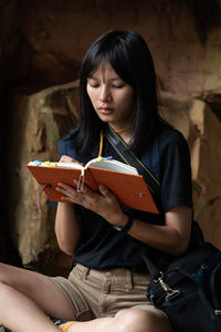 Young woman reading book while sitting in cave